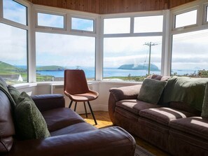 Ein Zimmer mit einem großen Fenster, einem braunen Ledersofa, einem braunen Sessel und einem grünen Zierkissen.