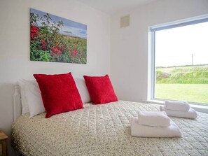 Ein Schlafzimmer mit einem Bett, zwei roten Kissen, einer weißen Decke und einem Blumenbild an der Wand.