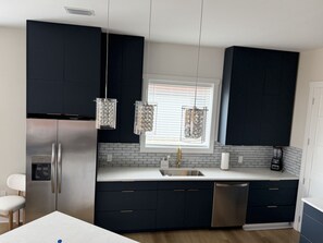 A modern kitchen with dark cabinetry, stainless steel appliances, and pendant lights. - Coastal Luxury Villa: Private Pool, TV Patio (Mexico Beach)