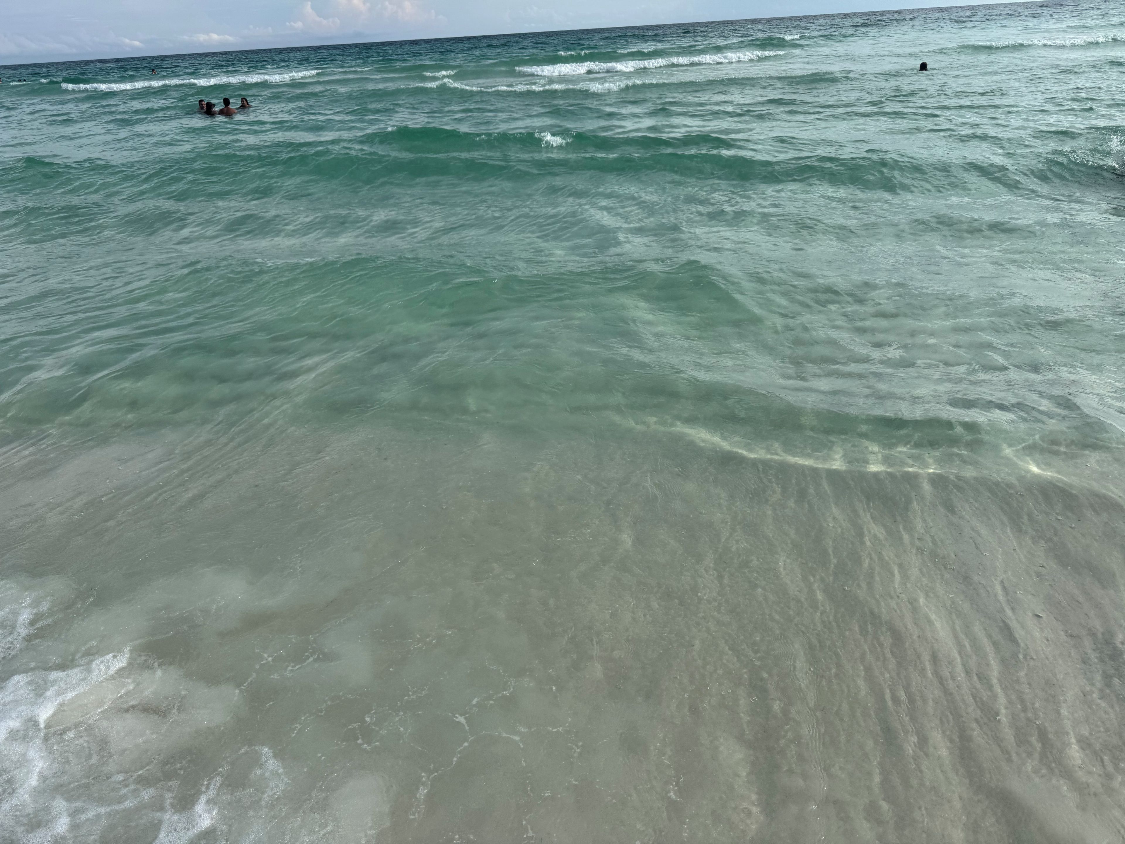 A beach with clear water and waves, and people swimming.