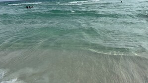 En strand med klart vatten och vågor, och folk som badar.