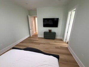 A bedroom with a bed, a TV, a dresser, and a door leading to another room. - Coastal Luxury Villa: Private Pool, TV Patio (Mexico Beach)