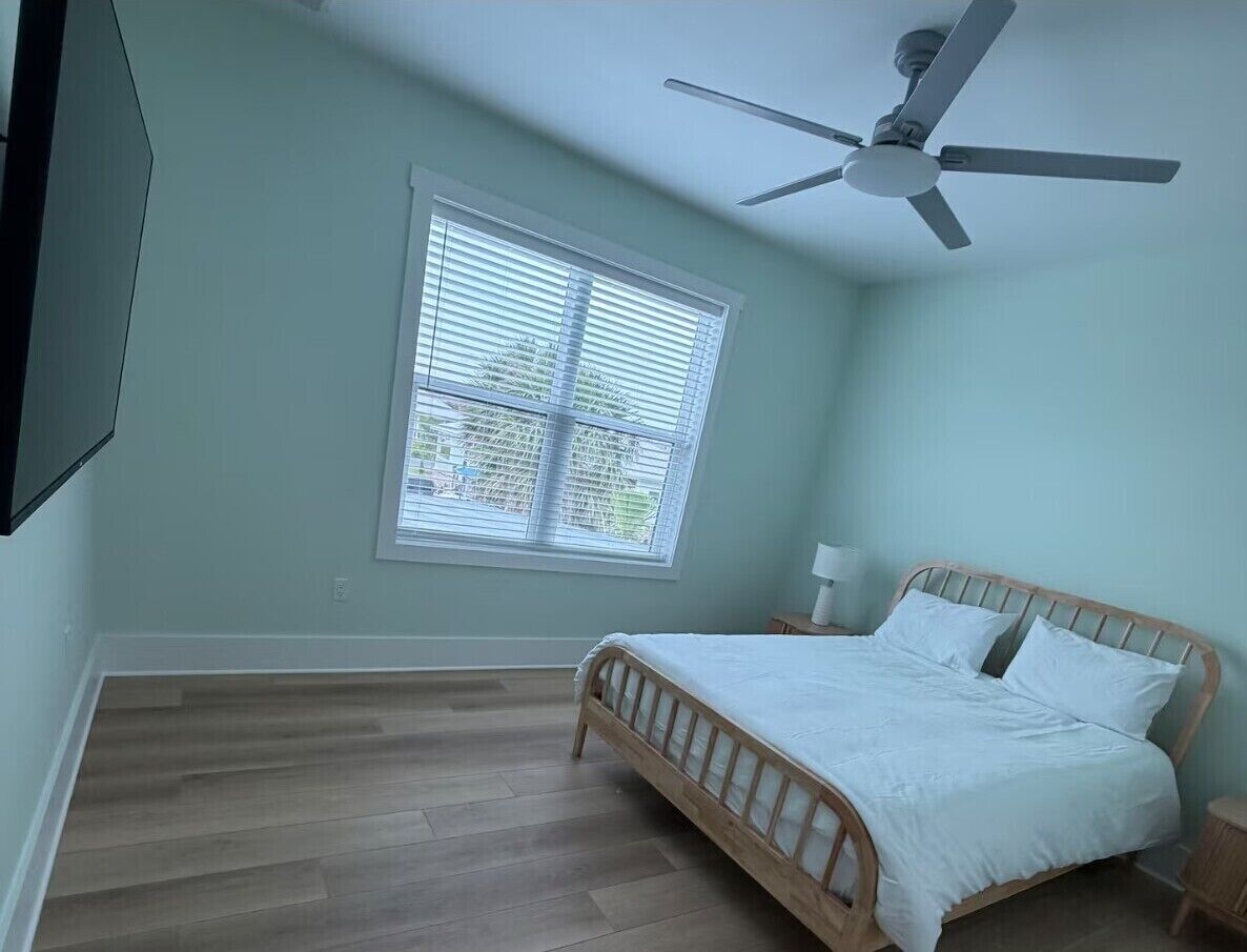 A bedroom with a bed, a ceiling fan, a window with blinds, and a wooden floor.