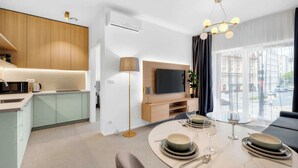 Una camera d'albergo moderna con angolo cottura, zona pranzo e un'ampia finestra con vista sulla città.