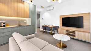Ein modernes Wohnzimmer mit einer Couch, einem Esstisch mit Stühlen, einem Fernseher und einer Küchenzeile mit Schränken und einer Arbeitsplatte.