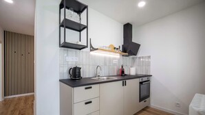 A modern kitchen with a black countertop, white cabinets, a built-in oven, and a black shelf above the sink.