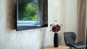 A flat-screen TV mounted on a wall, a dark-colored chair, and a vase with flowers on a wooden table.
