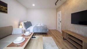 A modern hotel room with a bed, a TV, a dining table with plates and cutlery, and a bench.