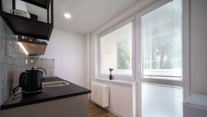 A modern kitchen with a black countertop, a kettle, and a window with blinds.