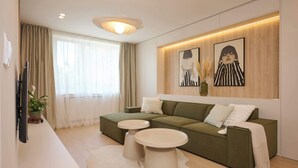 A modern living room with a green sofa, two round coffee tables, a flat-screen TV, and artwork on the wall.