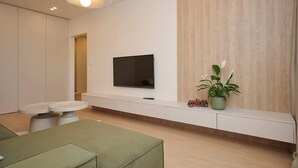 A modern living room with a flat-screen TV, a bench with potted plants, and a green sofa.