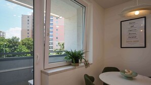 A room with a balcony, a dining table with chairs, a potted plant, and a framed menu on the wall.
