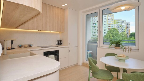 A modern kitchen with a built-in oven, a sink, and a dining area with a round table and green chairs.