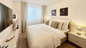 Een moderne slaapkamer met een bed, nachtkastjes, een televisie en kunst aan de muur.