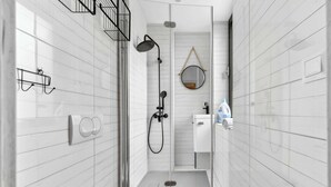 Ein schmales Badezimmer mit weiß gefliesten Wänden, einer Dusche mit Duschhandstück, einer Toilette und einem Waschbecken mit Spiegel darüber.