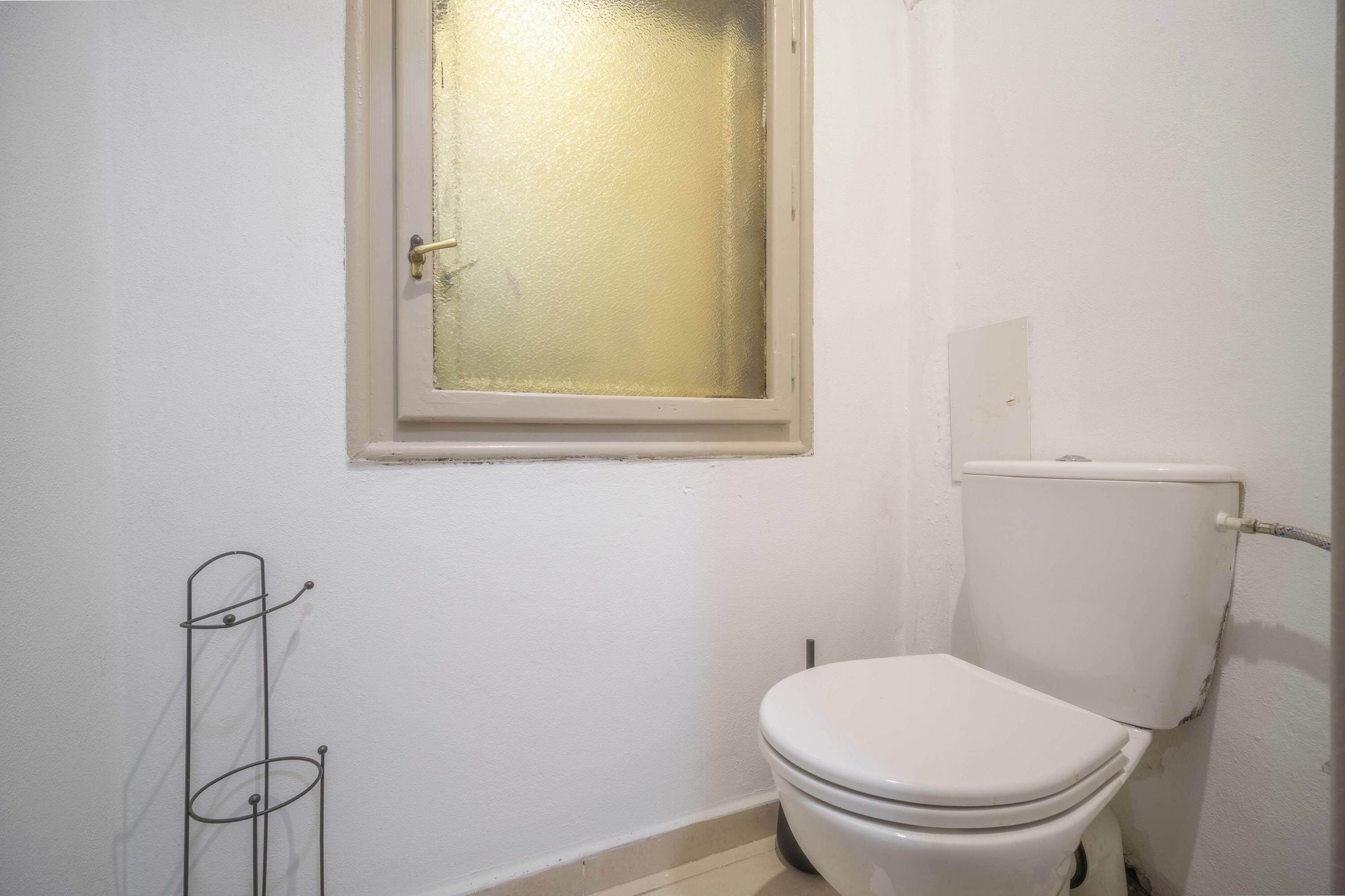 A small bathroom with a toilet, a window with a frosted glass door, and a metal towel rack.
