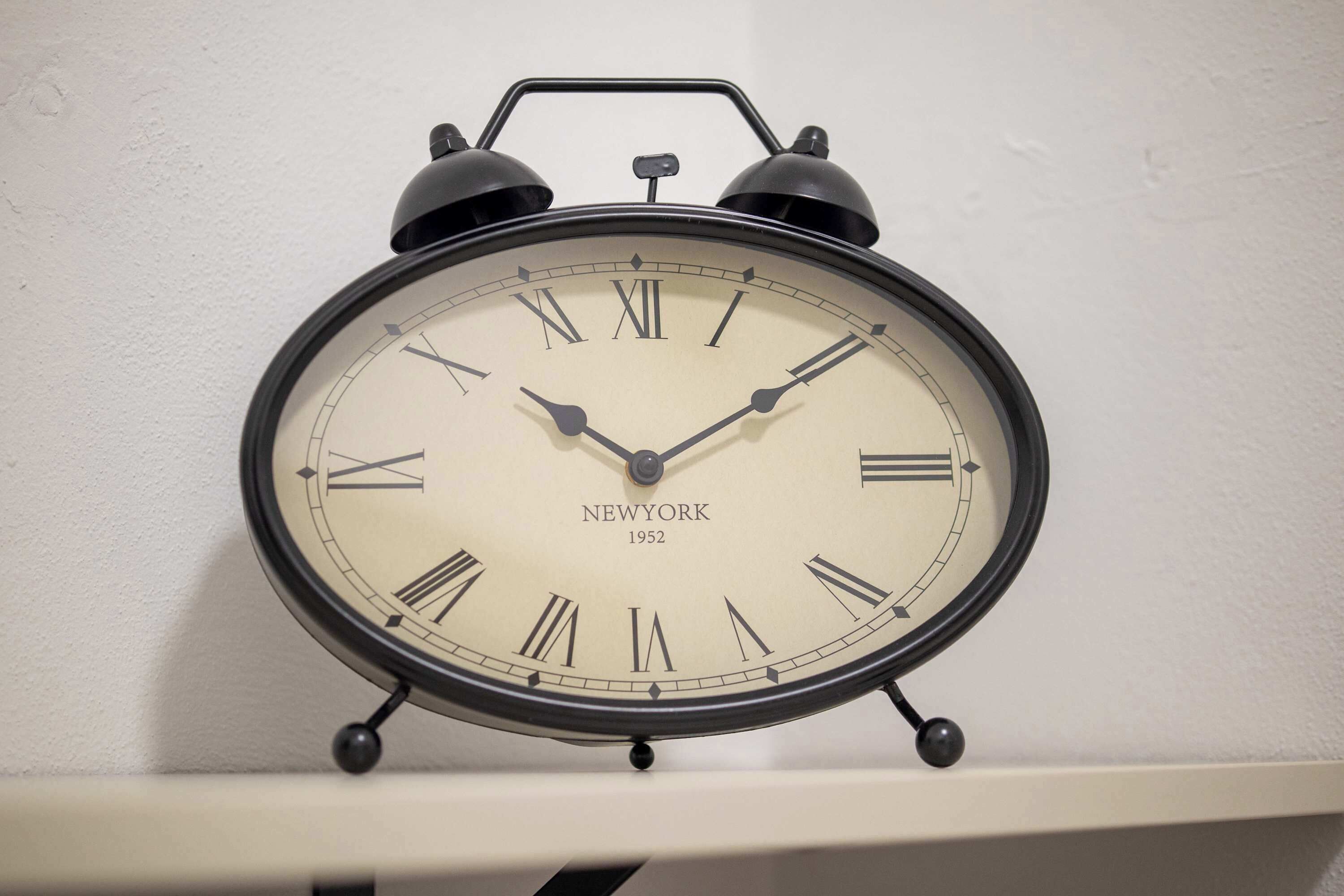 A black New York alarm clock with Roman numerals, mounted on a white wall.