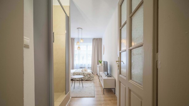 A hallway leading to a bedroom with a bed, bedside table, and a TV. - Elegant Studio in Historical Centrum | AC & Netflix (Košice I)