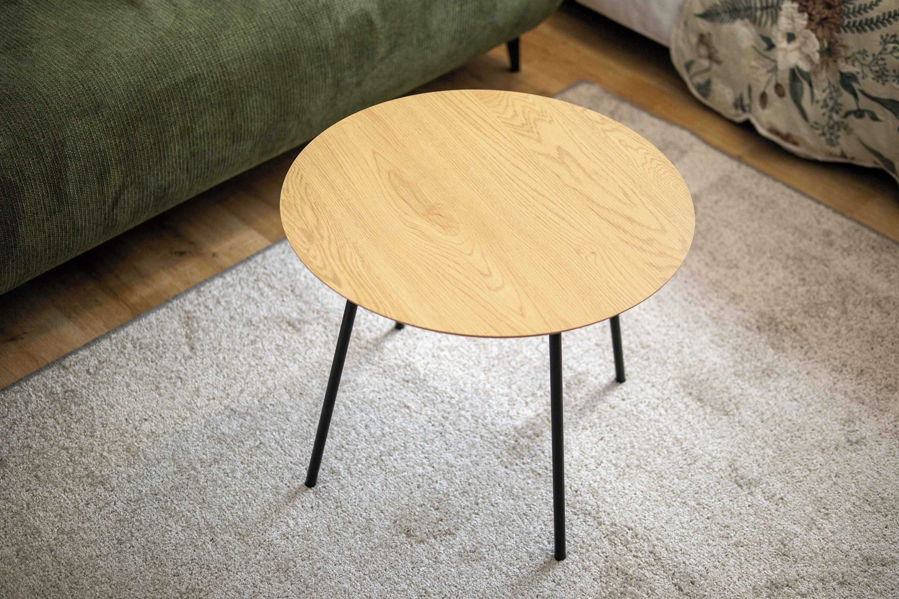 A round wooden table with black legs on a carpeted floor.
