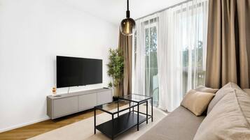 Una sala de estar moderna con un televisor de pantalla plana, una mesa de centro de vidrio, un sofá y un ventanal con cortinas.