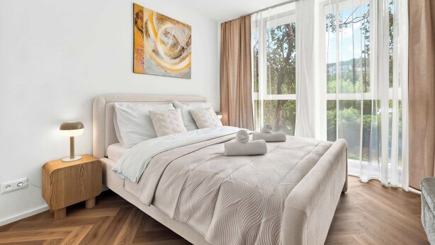 Ein Schlafzimmer mit einem Bett, einem Nachttisch, einer Lampe, einem Gemälde und einem Fenster mit Vorhängen.