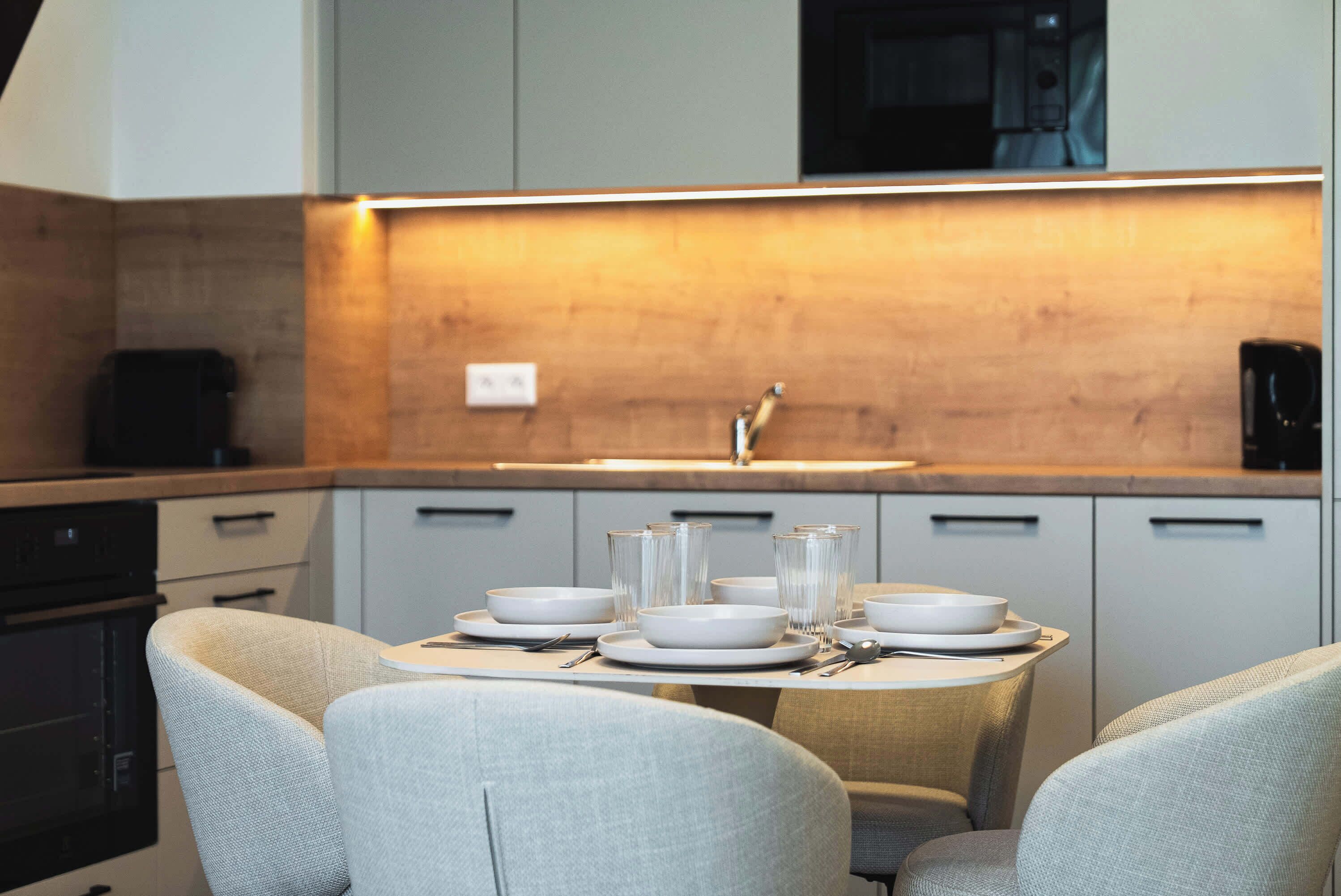 A modern kitchen with a dining table set for four, equipped with white plates, bowls, and glasses.