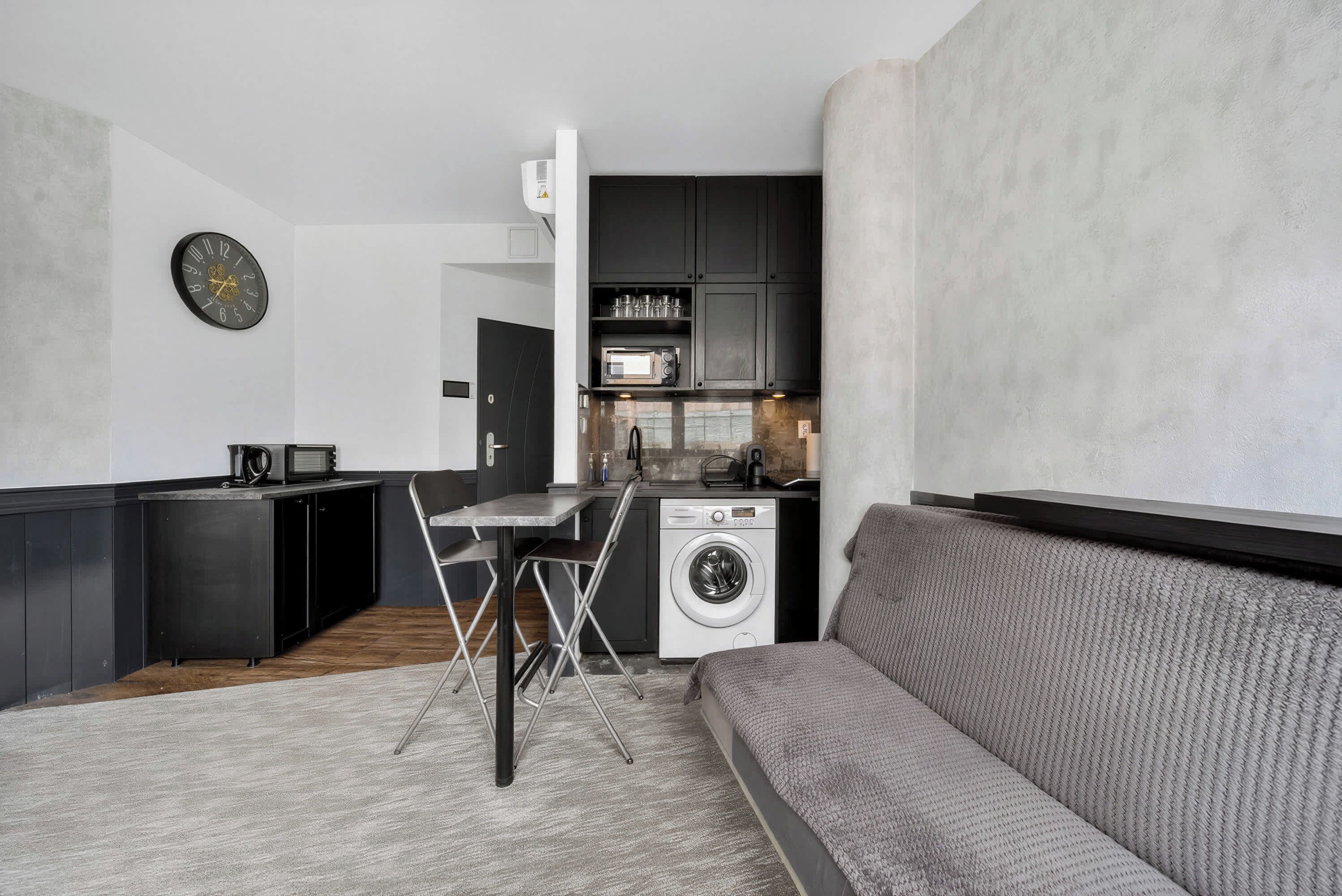 Un espace de vie compact comprenant un coin cuisine, un lave-linge, une table à manger avec des chaises et un canapé.