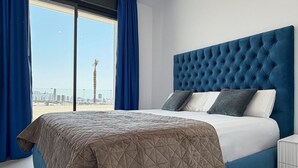 Una camera da letto con un letto grande, una testiera trapuntata e vista sulla città attraverso ampie finestre.
