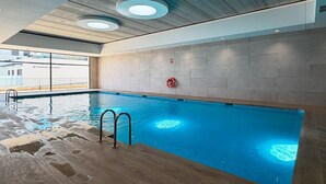 Una piscina interna con acqua cristallina, un solarium in legno e vista sull'esterno.