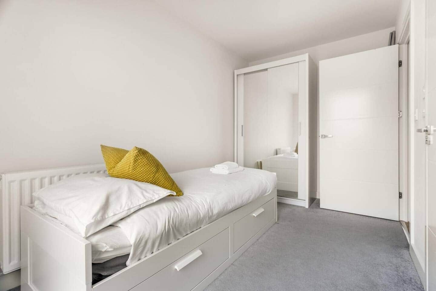 A white bed with two pillows, a bedside drawer, and a white radiator.