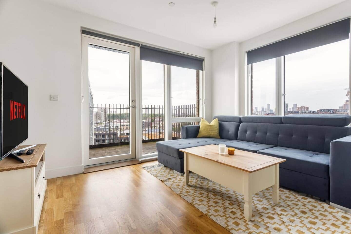Een moderne woonkamer met een bank, een salontafel, een televisie en een schuifdeur naar een balkon.