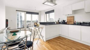 Une cuisine moderne avec des meubles blancs, un plan de travail noir et une vue sur la ville grâce à de grandes fenêtres.
