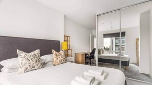 Une chambre d’hôtel avec un grand lit, deux oreillers, un bureau, une chaise et un miroir qui reflète une autre pièce.