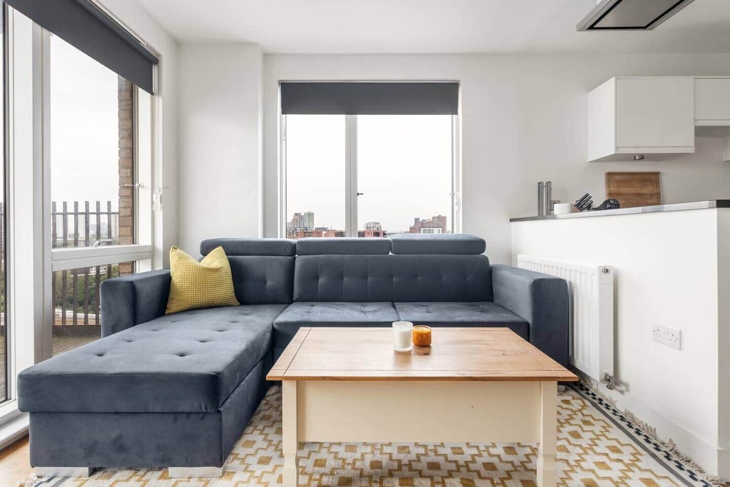 A modern living room with a sectional sofa, a wooden coffee table, and large windows offering a city view.