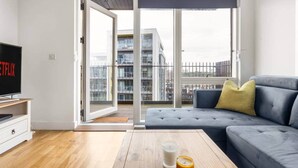 Un salon moderne avec un canapé, un téléviseur, une table basse ornée de bougies et une porte-fenêtre coulissante donnant sur un balcon extérieur.