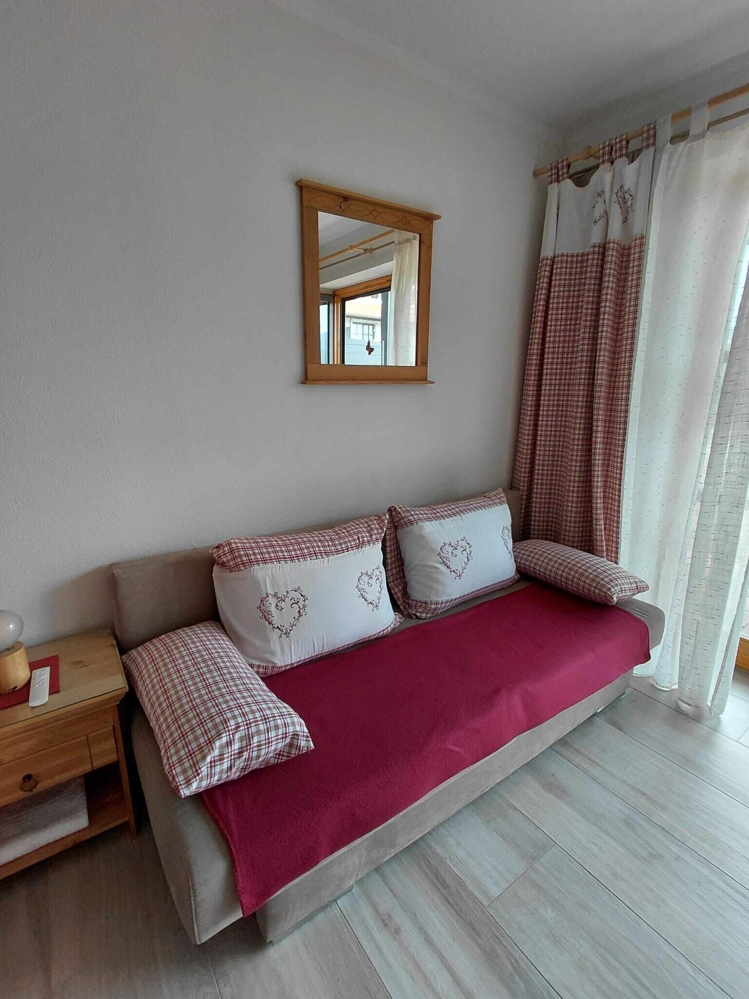 Ein Schlafzimmer mit Schlafsofa, Nachttisch mit Lampe und einem Fenster mit Vorhängen.