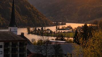 A church with a steeple, a body of water, and a hilly landscape.