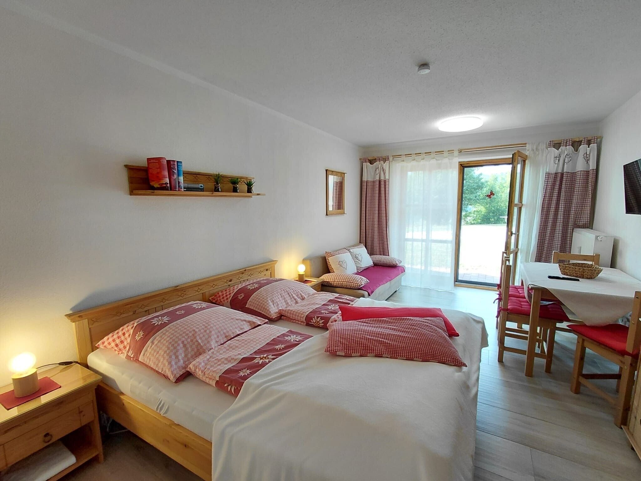 A bedroom with two beds, a desk, and a chair. There is a shelf with books and a small plant.