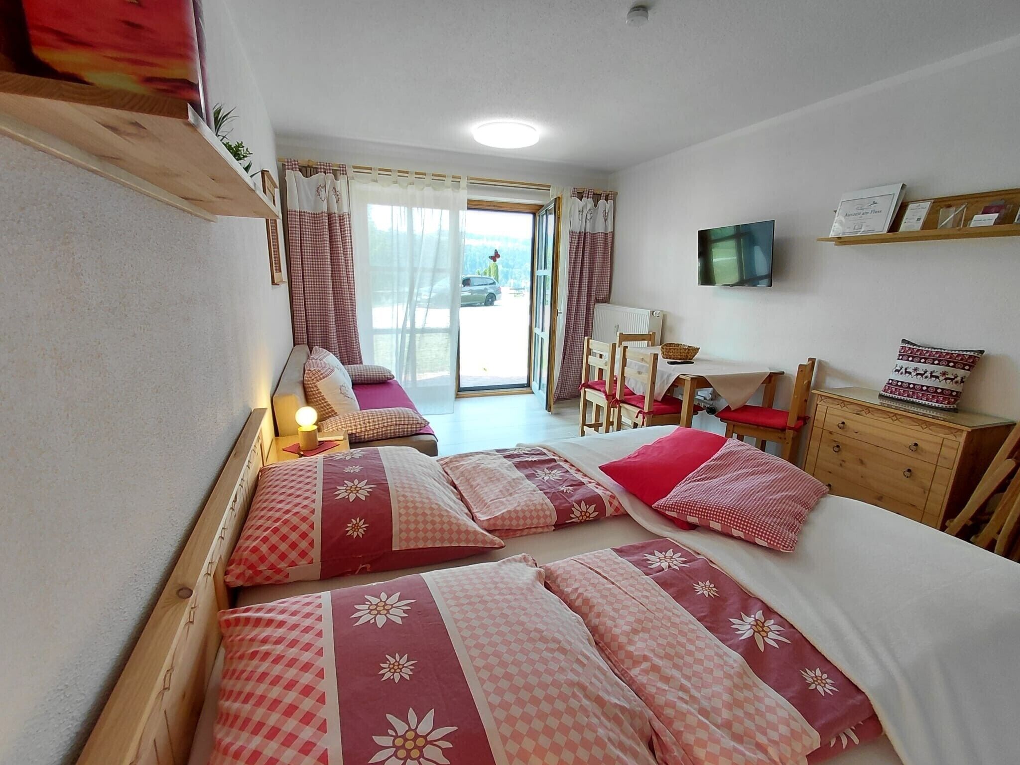 A room with two beds, a television, a wooden dresser, and a window with curtains.