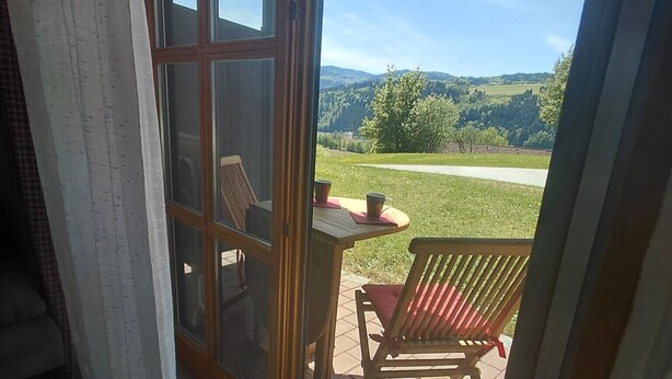 Una habitación con puerta de vidrio corrediza que da a un patio exterior con mesa, sillas y vistas a un paisaje verde.