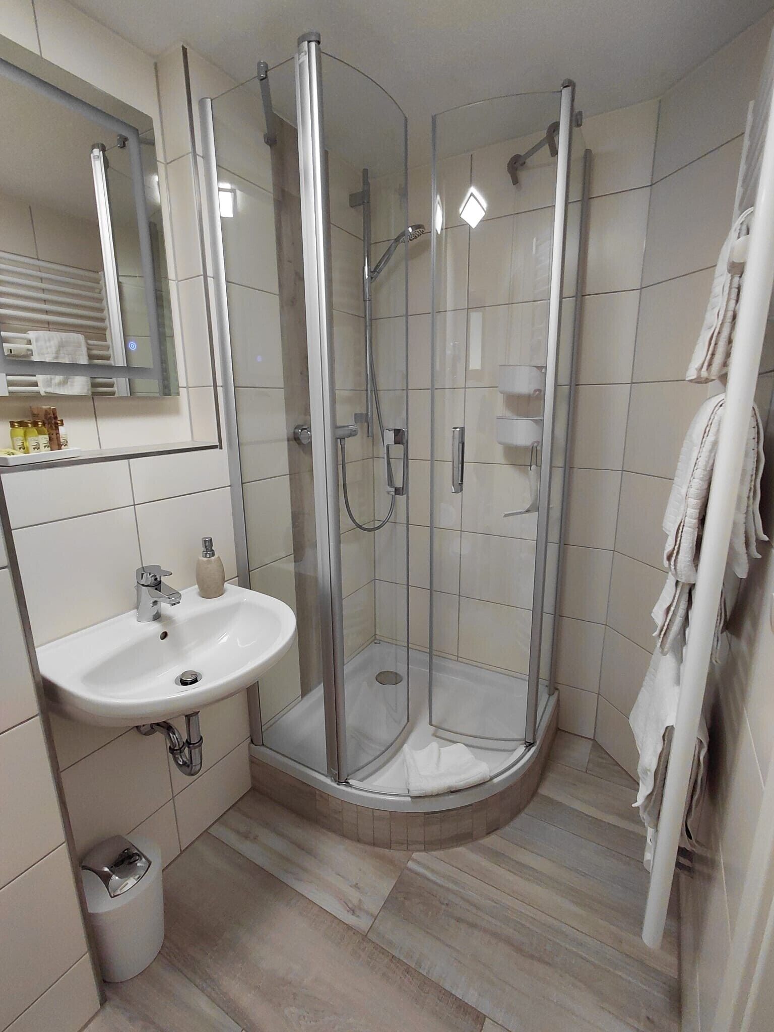 Ein modernes Badezimmer mit einer gläsernen Dusche, einem weißen Waschbecken und einem Spiegel darüber.