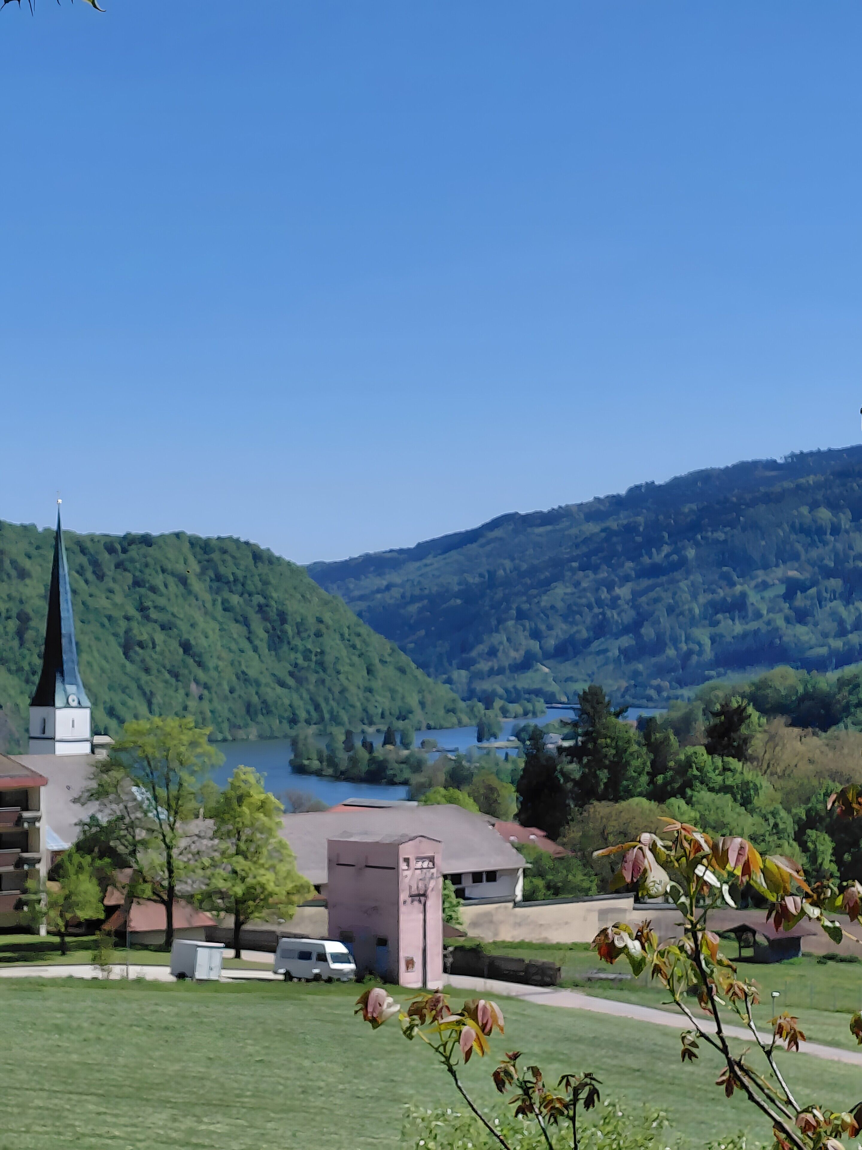 A church with a steeple, a small building, and a grassy area with trees.