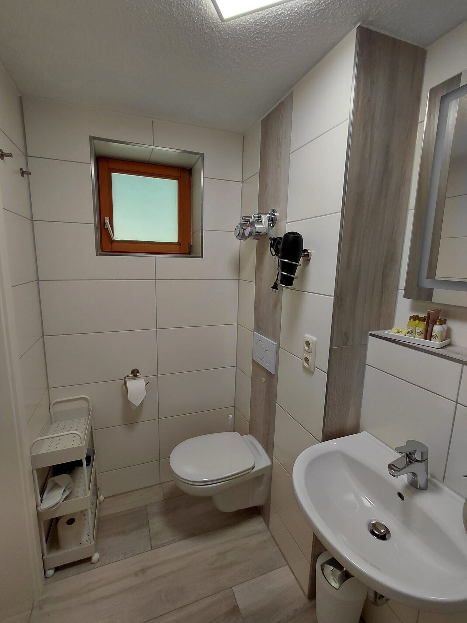 Une petite salle de bain avec des toilettes, un lavabo, un miroir et une fenêtre.