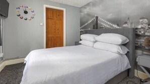 Une chambre avec un lit, une porte en bois et une fresque représentant un paysage urbain sur le mur.