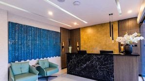 A modern reception area with a marble counter, two green chairs, and a decorative blue wall.
