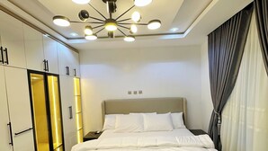 A modern bedroom with a large bed, a chest of drawers, a wardrobe, and a ceiling light fixture.