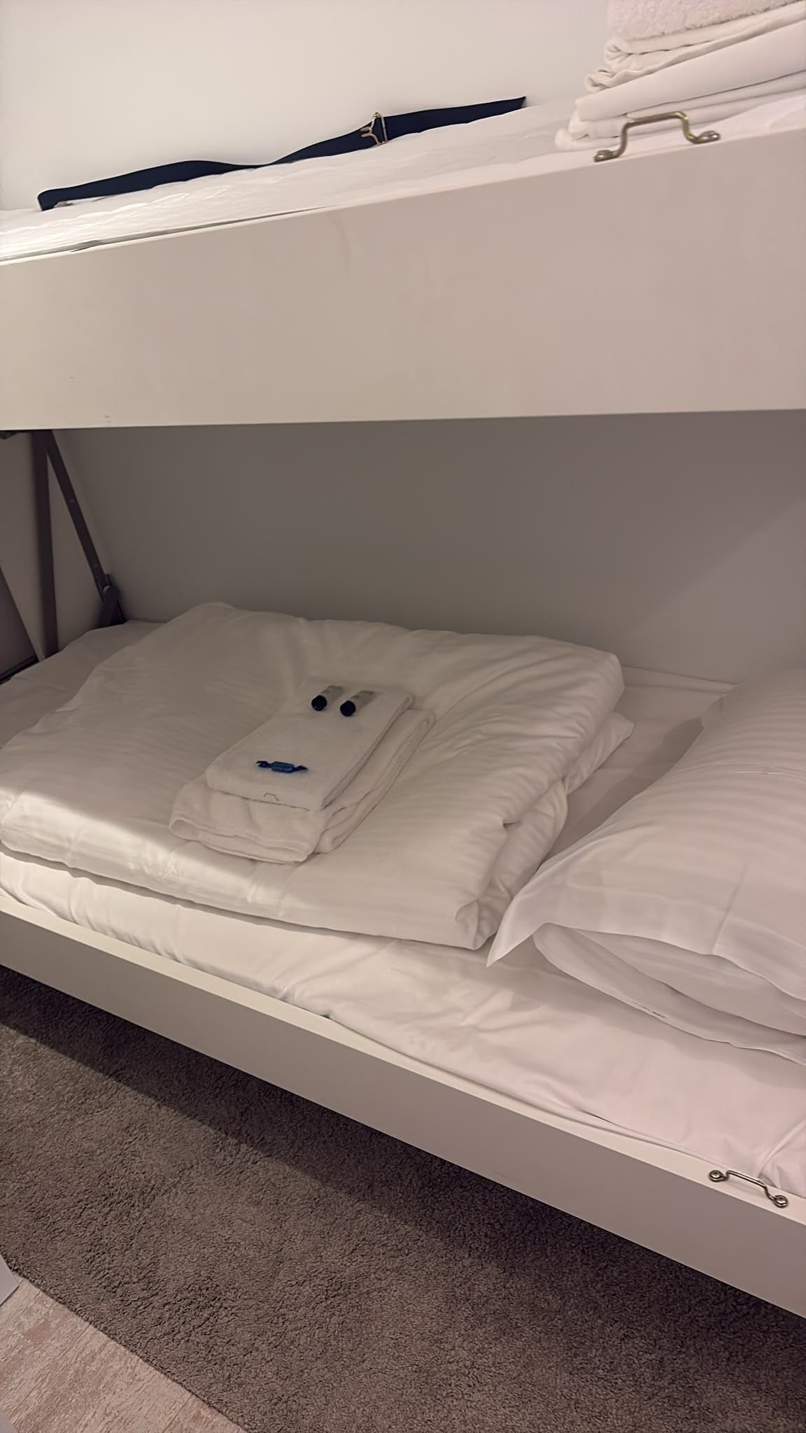 A bunk bed with white bedding and a folded towel on the lower bunk.