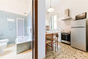 Een moderne badkamer met bad, toilet en douche. De keuken heeft een eettafel, stoelen, een koelkast en een oven.