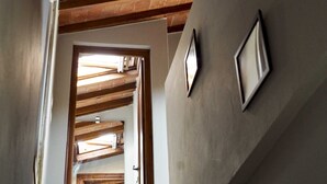 Ein Zimmer mit schrägverdeckter Decke, Holzbohlen, einer Tür zu einem anderen Raum und einer Wandleuchte.
