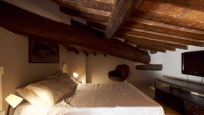 Ein Schlafzimmer mit einem hölzernen Bett, einem Nachttisch mit Lampe, einem Sessel, einem Fernseher und einer Steinwand.